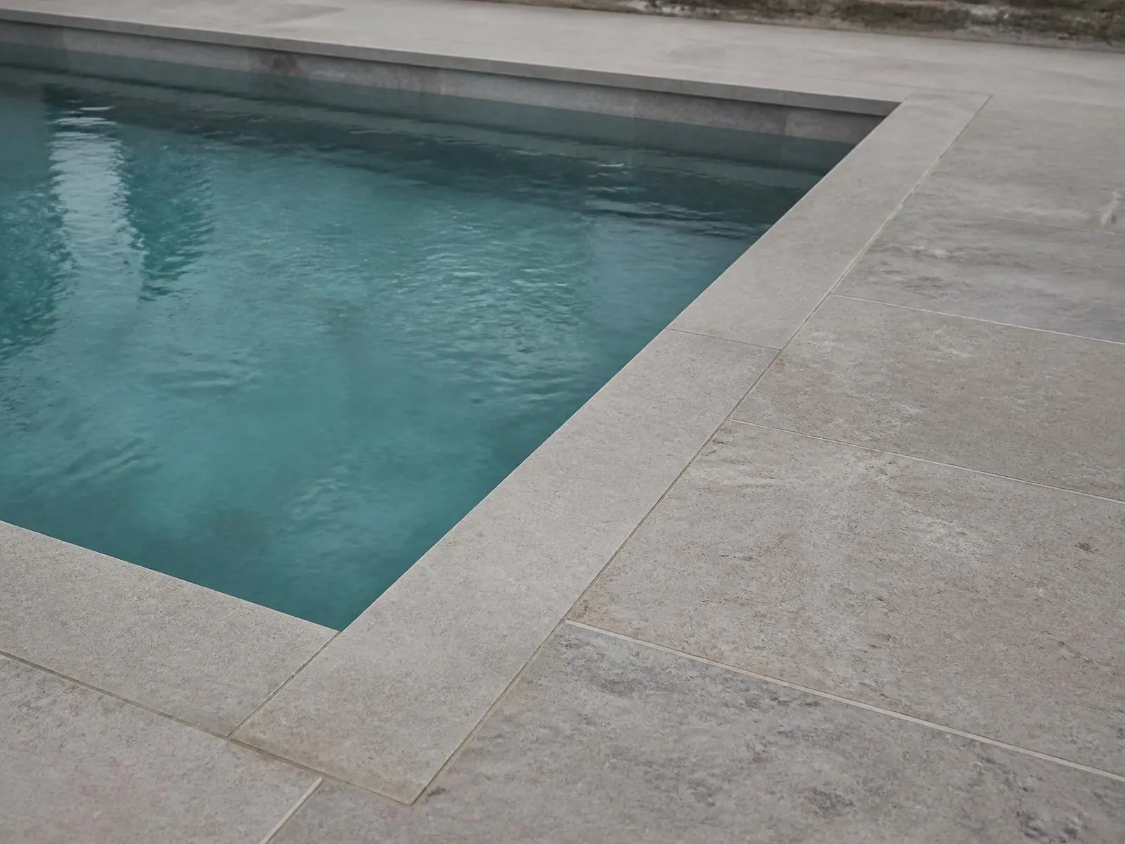 Indicative visualisation of pale limestone coping and paving around the edge of a swimming pool, still water alongside